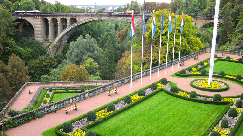 Lush green garden adorned with proudly hoisted Luxembourg and European Union flags and a charming arch bridge